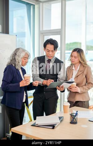 Verschiedene asiatische Geschäftsleute stehen in einem modernen Büro zusammen und konzentrieren sich auf die Arbeitsdiskussion. Ein junger, kluger asiatischer CEO zeigt es dem Finanzvertreter Stockfoto