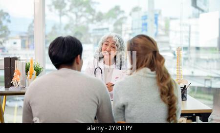 Eine professionelle asiatische Ärztin in Uniform mit einem jungen Ehepaar im Untersuchungsraum. Arztbesuch, Gesundheit Stockfoto