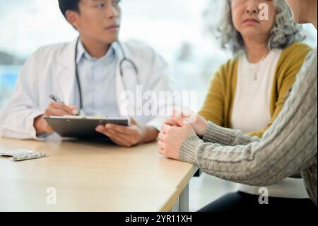 Eine Nahaufnahme einer fürsorglichen Tochter, die die Hand ihrer Mutter hält, um sie zu trösten, während sie sich mit dem Arzt berät und sich einer Untersuchung im Krankenhaus unterzieht. Stockfoto