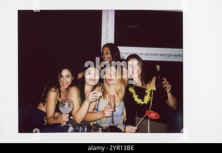 Eine fröhliche Gruppe von Freunden feiert einen Abend, aufgenommen in einer Vintage-Instant-Kamera. Stockfoto