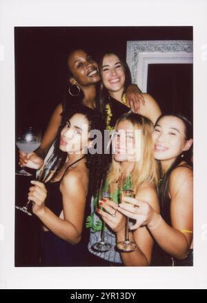 Vier Freunde auf einer Party, genießen Cocktails und halten den Moment mit einer sofortigen Kamera fest. Das Foto hat ein Retro-Feeling. Stockfoto