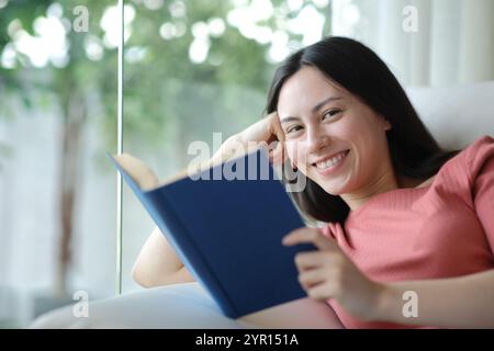 Glücklicher asiatischer Leser, der ein Papierbuch hält und dich zu Hause ansieht Stockfoto