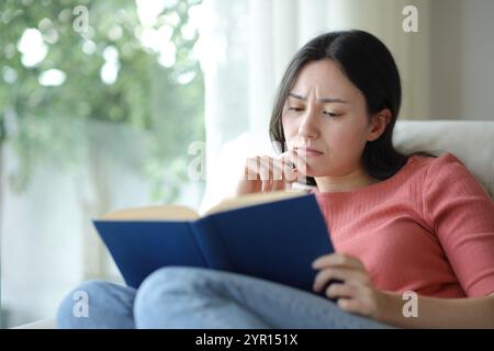 Traurige asiatische Frau, die ein Papierbuch liest und zu Hause auf einer Couch sitzt Stockfoto