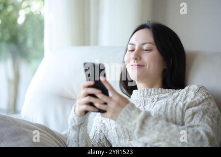 Zufriedene asiatische Frau, die zu Hause auf einem Sofa sitzt Stockfoto