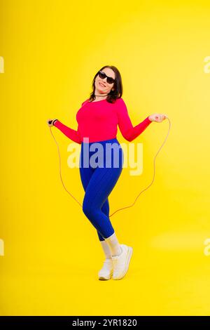 Hübsch lächelnde, pralle Frau in sportlichem Oberteil und Leggings, die ein Springseil in den Händen hält Stockfoto