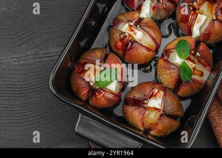Im Ofen gebackene Feigen mit Camembert- oder Brie-Käse, Kräutern und Honig. Gesundes Essen, saisonales Obst, leckerer Snack. Schwarzer Holzhintergrund, Draufsicht Stockfoto