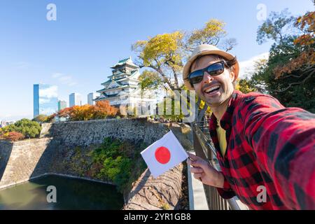 Mann junger Reisetourist macht ein Selfie mit japans Flagge auf Osaka Castle, Osaka Castle ist eines der berühmtesten Wahrzeichen in Japan und Osaka, Urlaub Stockfoto