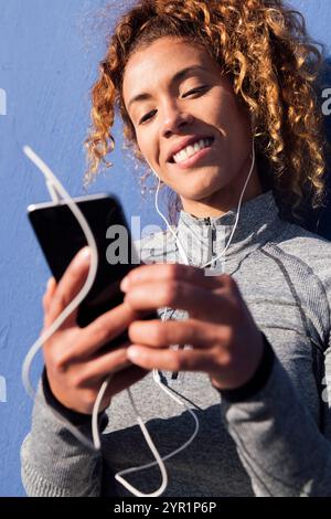 lateinische Frau in Ohrhörern mit Handy Stockfoto
