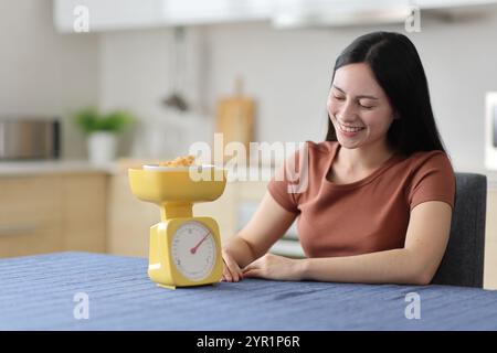 Glückliche asiatische Frau wiegt Müsli mit Waage in der Küche zu Hause Stockfoto