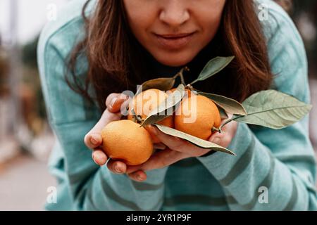 Frau, die frische Mandarinen mit Blättern in der Nähe hält Stockfoto
