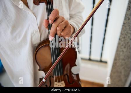 Eine detaillierte Ansicht eines Musikers, der eine Geige in einem Raum hält und die Hände und Saiten betont. Die Aufnahme fängt das Wesen der klassischen Musik ein Stockfoto