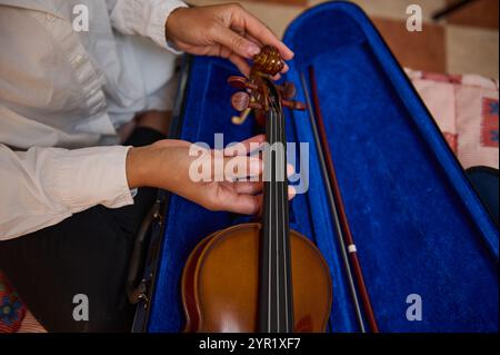Eine detaillierte Ansicht der Hände, die geschickt die Stimmstifte einer Geige anpassen, mit einem Bogen in einem leuchtend blauen Violingehäuse. Die Abbildung zeigt die PREC Stockfoto