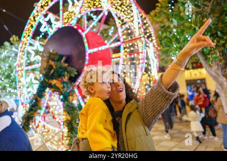 Mutter und Sohn bestaunen die festlichen Lichter der Stadt bei Nacht und schaffen eine fröhliche Urlaubsatmosphäre. Sie teilen Liebe, Freude und Aufregung Stockfoto