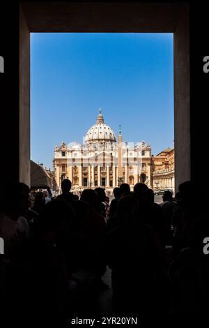 Besucher treffen sich im Vordergrund, während sie an klaren Tagen den atemberaubenden Petersdom in der Vatikanstadt bewundern. Stockfoto