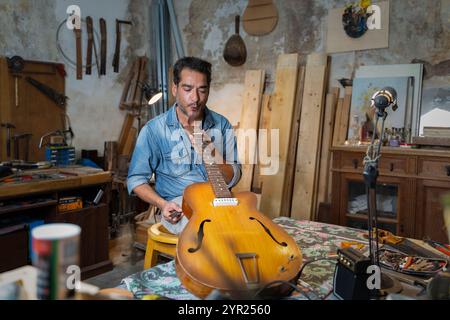 Erfahrener Geigenbauer, der in authentischer Werkstatt an Akustikgitarre arbeitet. Erfahrener Handwerker, der alte Musikinstrumente mit traditionellen Werkzeugen repariert Stockfoto