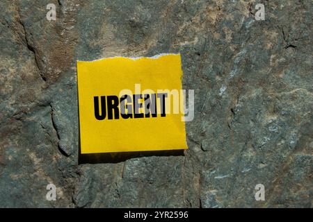 Dringende Nachricht geschrieben auf gerissenem gelbem Papierstück mit Steinhintergrund. Konzeptionelles dringendes Wortsymbol. Kopierbereich. Stockfoto