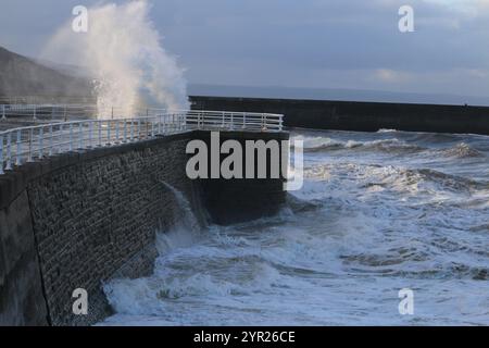 Aberystwyth Wales UK Wetter 2. Dezember 2024. Ein kalter, stürmischer Wintermorgen an der walisischen Küste, große Wellen krachen über die Seeschützung und Hafenlicht mit rosa Himmel über der Küste, Credit: mike davies/Alamy Live News Stockfoto