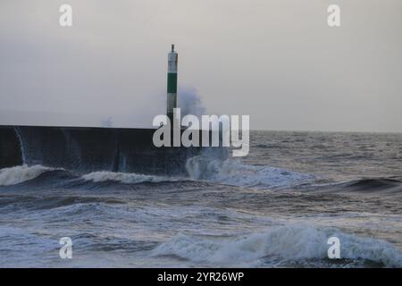 Aberystwyth Wales UK Wetter 2. Dezember 2024. Ein kalter, stürmischer Wintermorgen an der walisischen Küste, große Wellen krachen über die Seeschützung und Hafenlicht mit rosa Himmel über der Küste, Credit: mike davies/Alamy Live News Stockfoto