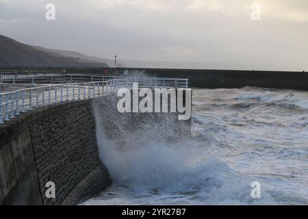 Aberystwyth Wales UK Wetter 2. Dezember 2024. Ein kalter, stürmischer Wintermorgen an der walisischen Küste, große Wellen krachen über die Seeschützung und Hafenlicht mit rosa Himmel über der Küste, Credit: mike davies/Alamy Live News Stockfoto