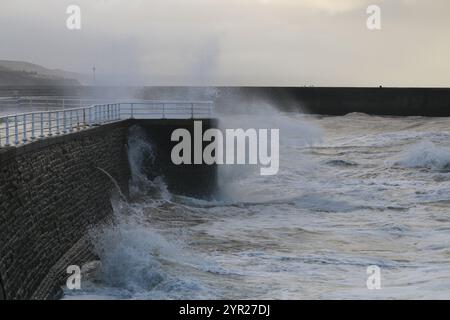 Aberystwyth Wales UK Wetter 2. Dezember 2024. Ein kalter, stürmischer Wintermorgen an der walisischen Küste, große Wellen krachen über die Seeschützung und Hafenlicht mit rosa Himmel über der Küste, Credit: mike davies/Alamy Live News Stockfoto