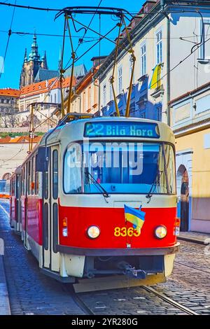 Die alte rote Straßenbahn fährt entlang der schmalen Letenska-Straße, vorbei an historischen Häusern mit dem Veitsdom, der die Skyline von Prag, Tschechien dominiert Stockfoto