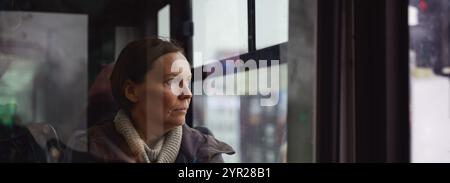 Traurige und besinnliche Frau, die mit einem schmutzigen Bus durch die Straßen der Stadt fährt, selektiver Fokus Stockfoto