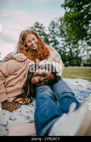 Glückliches Teenager-Mädchen, das auf weiblichen Freundinnen im Park schläft Stockfoto