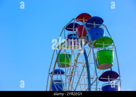 Farbenfrohes Riesenrad mit roten, blauen, grünen Gondeln vor hellblauem Himmel. Stockfoto