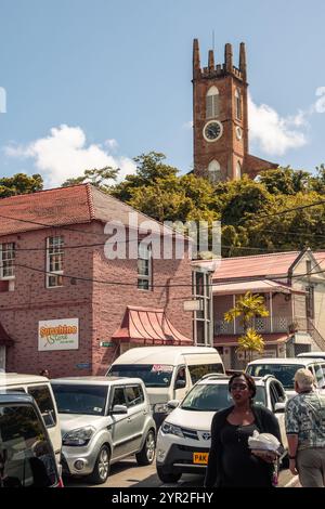 St. George's, Grenada - 4. Januar 2018: Eine geschäftige Straßenszene mit historischer Architektur und einem prominenten Kirchturm im Hintergrund. Stockfoto
