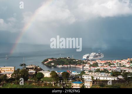 St. George's, Grenada - 4. Januar 2018: Ein Regenbogenbogen über dem Hafen, während ein Kreuzfahrtschiff in der Nähe der farbenfrohen Stadt anlegt. Stockfoto