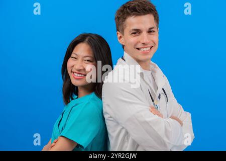 Lächelnde Mediziner stehen Rücken an Rücken auf blauem Hintergrund Stockfoto