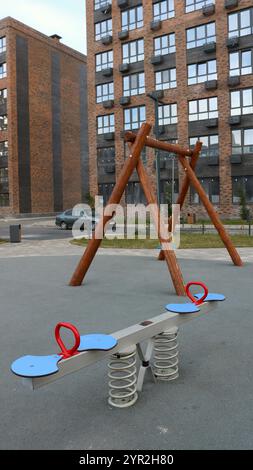 Kinderspielplatz im Innenhof eines Wohnkomplexes aus braunem Backstein mit Schaukeln aus natürlichen Materialien, vertikalem Shot, Spielbereich Stockfoto