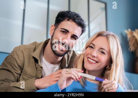 Glückliches Paar mit Schwangerschaftstest mit positivem Ergebnis im häuslichen Setting. Stockfoto