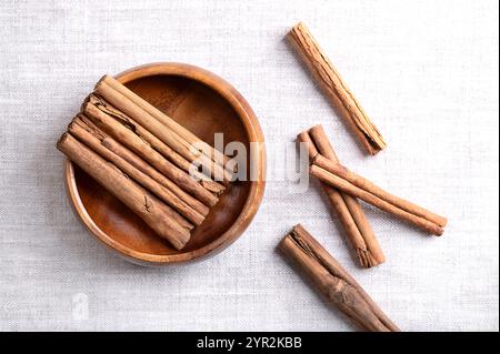 Ceylon-Zimt steckt in einer Holzschale auf Leinenstoff. Parallel angeordnete ganze, getrocknete Rindenstreifen von Cinnamomum verum. Stockfoto