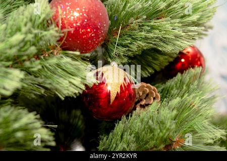 Weihnachtsschmuck hängt an einem üppig grünen Tannenzweig, verziert mit funkelnden Dekorationen. Festliche rote, goldene und silberne Kugeln sorgen für einen warmen Urlaub Stockfoto