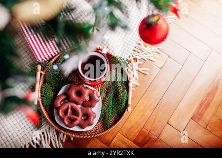 Hintergrund zum Neujahr. Tablett mit Kaffee und Schokoladenkuchen unter einem geschmückten Weihnachtsbaum mit Geschenkverpackungen. Blick von oben auf festliche Feiertagsgetränk. Stockfoto