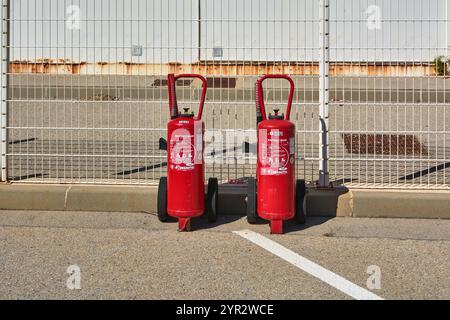 Marseille. Frankreich - 30. November 2024: Zwei industrielle rote Feuerlöscher auf Rädern werden vor einem Metallzaun in einem gepflasterten Außenbereich aufgestellt. Stockfoto