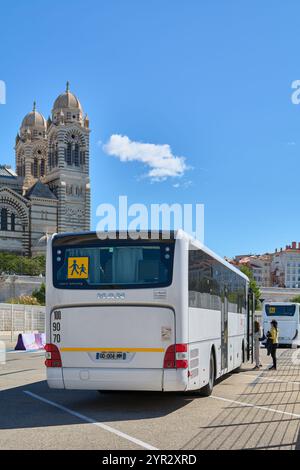 Marseille. Frankreich - 02. Dezember 2024: Das Bild zeigt einen weißen Überlandbus, der vor einer historischen Kathedrale in Marseille geparkt ist und die Tiere erfasst Stockfoto