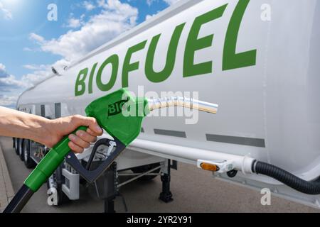 Hand mit Kraftstoffdüse mit Aufschrift BIO auf einem Hintergrund eines Tankwagens mit Biokraftstoff. CO2-neutrales Biokraftstoff-Dekarbonisierungskonzept. Stockfoto