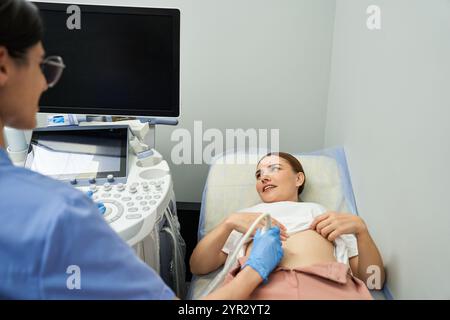 Ein Gynäkologe in einem Labormantel führt einen Ultraschall bei einer Patientin in einer medizinischen Umgebung durch. Stockfoto