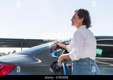 Eine Frau hält eine Wasserstofftankdüse an einer Wasserstofftankstelle. Auto mit Wasserstoff betanken. Stockfoto