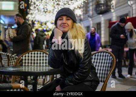 Eine Winterszene mit einer Frau, die eine Tasse heißes Getränk in einem gemütlichen Straßencafé genießt. Der Hintergrund zeigt eine festliche Straße, die von New beleuchtet wird Stockfoto