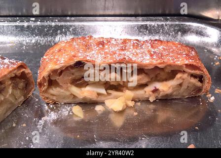 Apfelstrudel mit Rosinen und Puderzucker. Apfelstrudel ist eine weit verbreitete Strudelart. Zur Zubereitung werden vor allem sogenannter Strudelteig, aber auch Blätterteig, Quarkteig, österreichisch für Topfenteig und Hefeteig bzw Germteig verwendet. Ein aus Strudelteig zubereiteter Apfelstrudel wird, vor allem, wenn der Teig manuell zu einem Teigblatt ausgezogen wurde, ausgezogener Apfelstrudel genannt. Diese Variante ist in Österreich und anderen Gebieten der ehemaligen k u k Donaumonarchie eine traditionelle Mehlspeise bzw ein Nationalgericht *** Apfelstrudel mit Rosinen und Pulverzucker Stockfoto