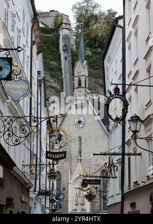 Salzburg, Österreich - 1. Oktober 2024: Bezaubernder Blick auf die Getreidegasse mit historischer Blasiskirche und traditionellen Schildern aus Schmiedeeisen Stockfoto