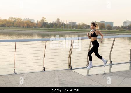 Ein entschlossener Läufer wandert selbstbewusst auf einem Flussweg und umhüllt die frische Morgenluft, mit der Skyline der Stadt und den Herbstbäumen, die ein Bild bilden Stockfoto