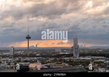 Eine Stadtlandschaft bei Sonnenuntergang mit dramatischen Wolken, einem markanten Fernsehturm, modernen Wolkenkratzern und einer weitläufigen urbanen Umgebung. Der Horizont zeigt Wind tur Stockfoto