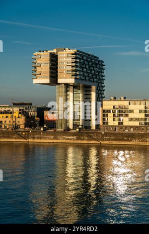 Modernes Gebäude am Fluss mit einzigartigem architektonischem Design reflektiert das ruhige Wasser unter einem klaren blauen Himmel. Das warme Sonnenlicht hebt seine Struktur hervor Stockfoto