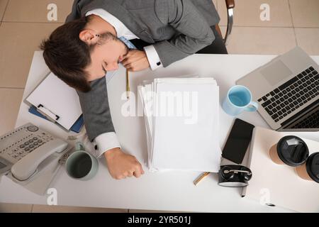 Stressiger Geschäftsmann, der am Tisch im Büro schläft, Blick von oben Stockfoto
