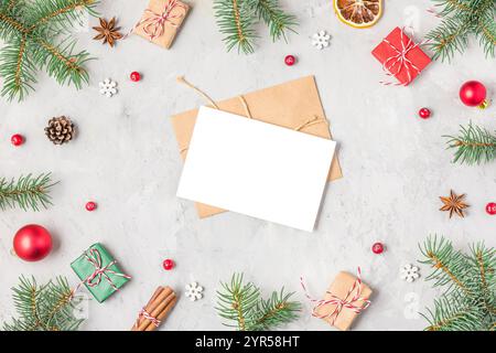 Weihnachtsgrußkarte im Rahmen aus Tannenzweigen, roten Dekorationen, Geschenkboxen, Weihnachtsessen und Tannenzapfen auf grauem Betonhintergrund. Flach Stockfoto