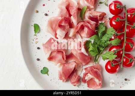 In Scheiben geschnittener Schinken, Vorspeise, mit Kirschtomaten, auf einem weißen Teller, Blick von oben Stockfoto